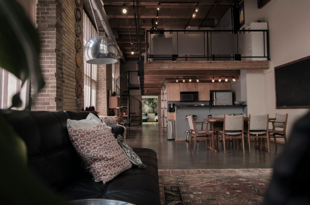 Industrial loft interior with exposed brick walls, open ceiling beams, metal accents, and modern furniture.